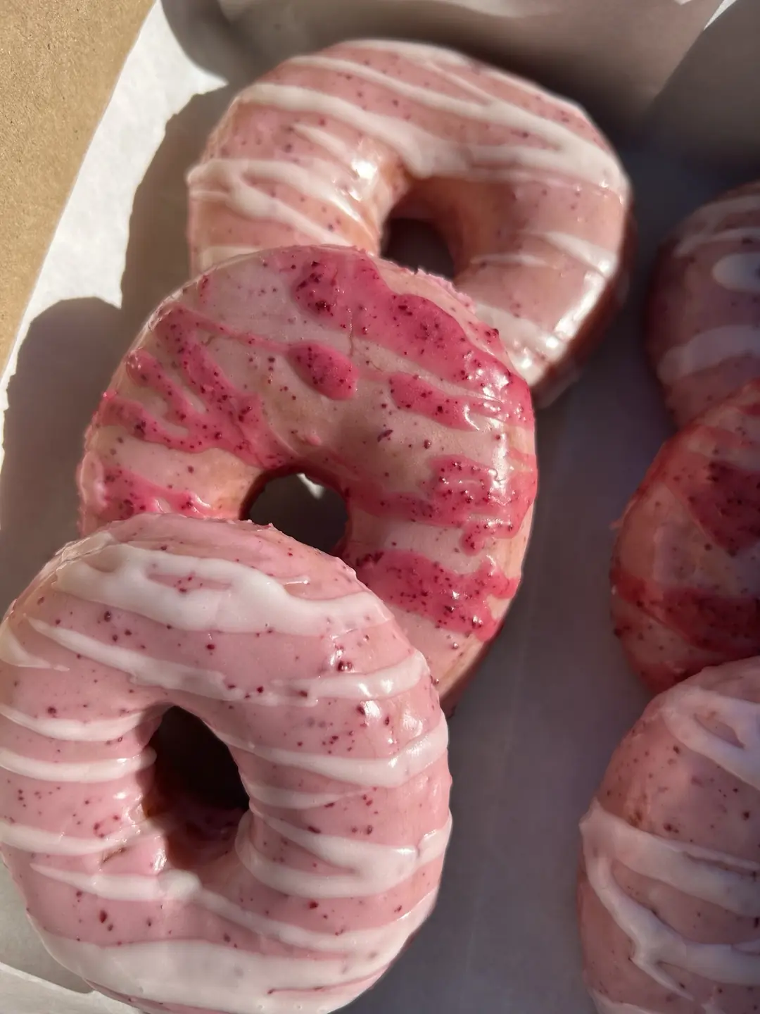 Pink berry-glazed plant-based donuts with a decorative drizzle from Mina's Kitchen